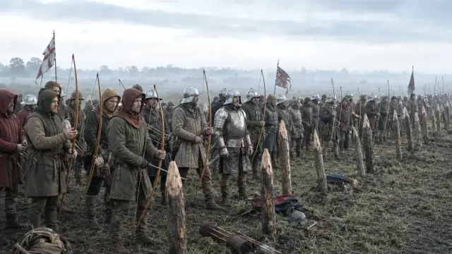 Reconstruction of the English line at Agincourt: archers behind a fence of angled stakes on ploughed wet ground, banners in the mist behind.