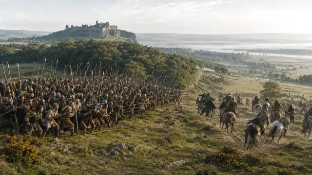 Reconstruction of a Scottish schiltron — a dense block of spearmen — advancing over open ground with Stirling Castle on its crag in the distance.