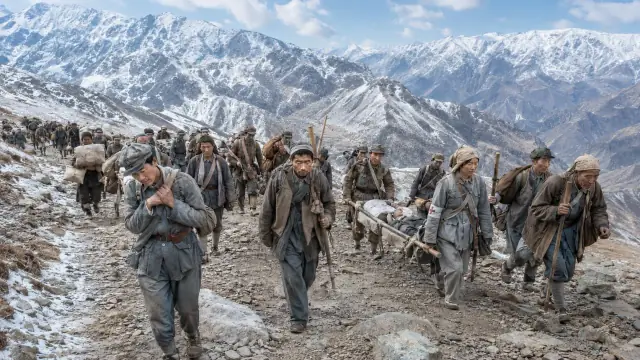 Reconstruction of a Long March column crossing a snow pass, marchers carrying a stretcher along a track between grey ridges.