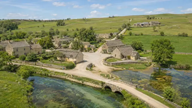 Aerial reconstruction of a Cotswold village of honey-coloured limestone, a clear stream running under a low bridge between the cottages.
