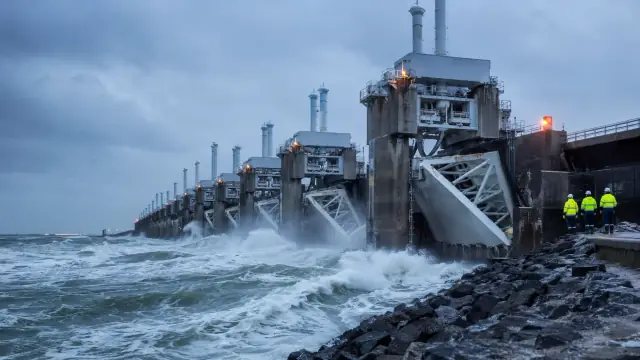 Reconstruction of a Dutch storm-surge barrier closing against a rising sea, water breaking white against the piers with engineers on the deck above.