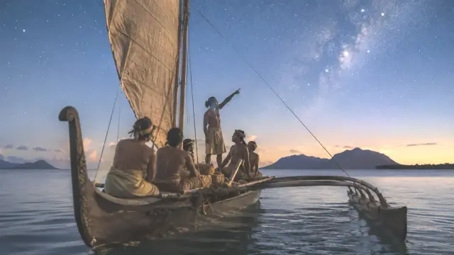 Reconstruction of a double-hulled voyaging canoe under sail at night, crew on the deck as the navigator sights along the horizon beneath a dense star field.
