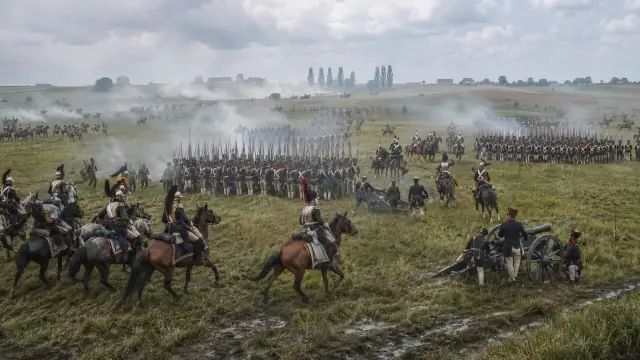 Reconstruction of Waterloo: infantry formed in squares on open rye ground with cavalry wheeling around them through drifting smoke.